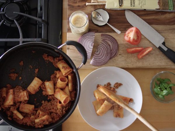 busy kitchen with vegetables on cutting board and pasta in a pot